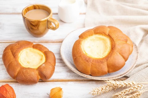 Sour cream bun with cup of coffee on a white wooden background and linen textile. Side view, close