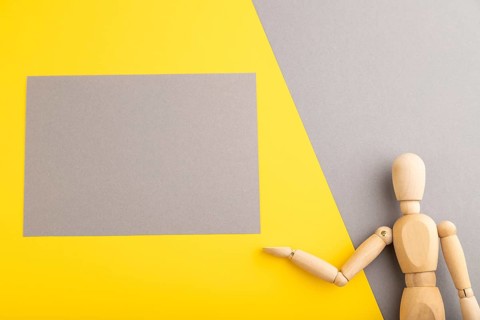 Wooden mannequin holding gray blank poster on gray and yellow pastel background. copy space,