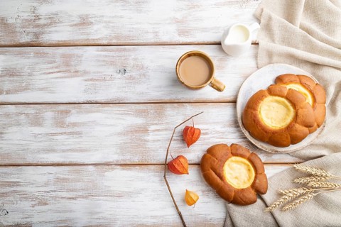 Sour cream bun with cup of coffee on a white wooden background and linen textile. top view, flat