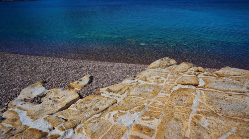 Rocky coast with pebbles and clear blue water under a blue sky, Lambi beach, pebble beach, Patmos,