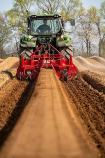 A farmer builds asparagus ridges on a field with the help of an asparagus tiller, in which the