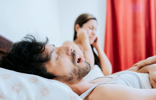 Snoring man in bedroom and wife covering her ears. Husband snoring while the wife suffers and