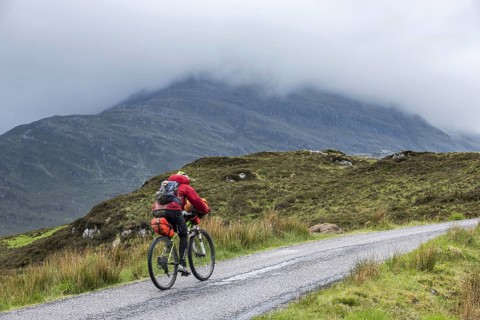 Lonely biker cycling through the Scottish Highlands on heavily laden touring bicycle along single