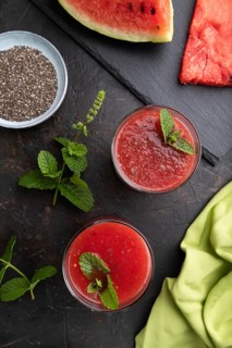 Watermelon juice with chia seeds and mint in glass on a black concrete background with green
