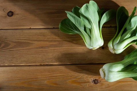 Fresh green bok choy or pac choi chinese cabbage on a brown wooden background. Hard light, contrast