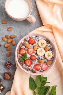 Chocolate cornflakes with milk, strawberry and almonds in ceramic bowl on gray concrete background