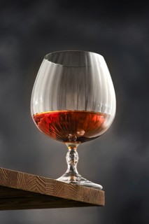 Facetted glass with brandy, quarter-filled with amber cognac stands on a rustic wooden shelf