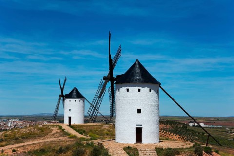 Two white windmills on a hill overlooking a vast landscape under a blue sky on a sunny day, Alcazar