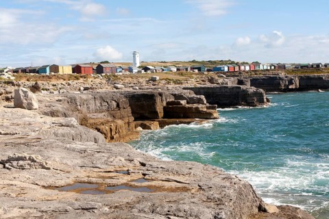 Old white lighthouse now a bird observatory and beach huts on the coast at Portland Bill, Isle of