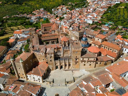 Aerial view of an old monastery with red roofs, surrounded by a village and green hills, presenting