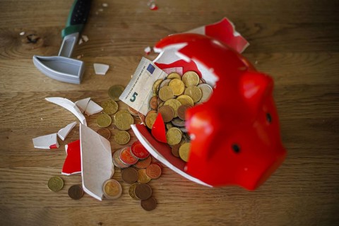 Symbolic photo on the subject of saving. An open, broken piggy bank with coins and banknotes stands