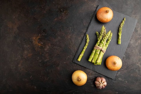 Bunch of fresh green asparagus, garlic, onion on slate board on black concrete background. Top