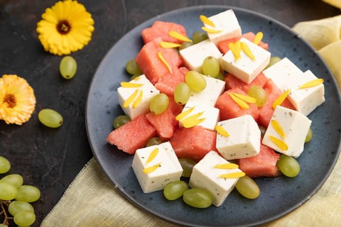 Vegetarian salad with watermelon, feta cheese, and grapes on blue ceramic plate on black concrete