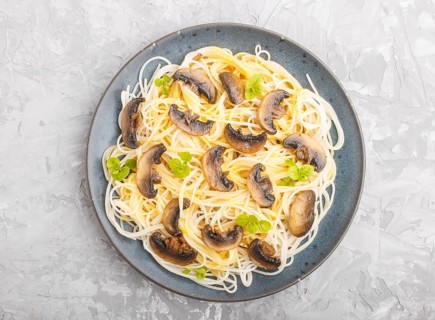 Rice noodles with champignons mushrooms, egg sauce and oregano on blue ceramic plate on a gray