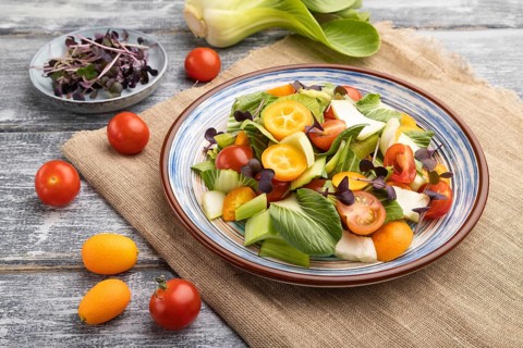 Vegetarian salad of pac choi cabbage, kiwi, tomatoes, kumquat, microgreen sprouts on gray wooden