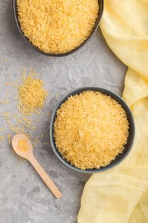 Blue ceramic bowl with raw golden rice and wooden spoon on a gray concrete background and yellow