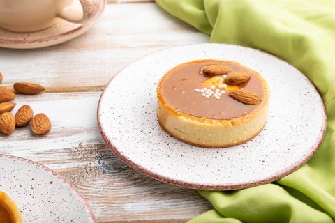 Sweet tartlets with almonds and caramel cream with cup of coffee on a white wooden background and
