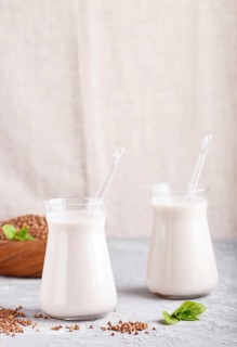 Organic non dairy buckwheat milk in glass and wooden plate with buckwheat seeds on a gray concrete