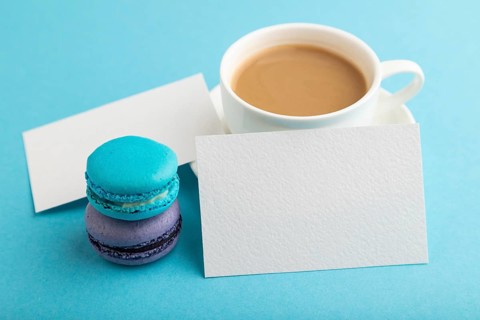 White paper business card mockup with blue and violet macaroons and cup of coffee on blue pastel