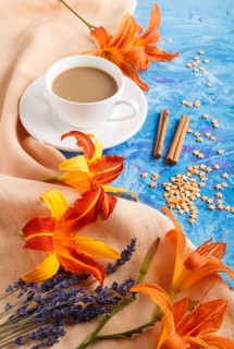 Orange day-lily and lavender flowers and a cup of coffee on a blue concrete background, with orange