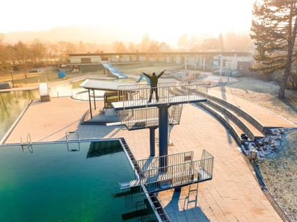A person stands on a diving platform in a swimming pool at sunrise in winter, ENCW outdoor pool