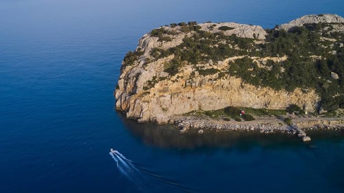 Drone shot, A rocky seashore with a small boat, calm water and a cloudless sky, Anthony Quinn Bay,