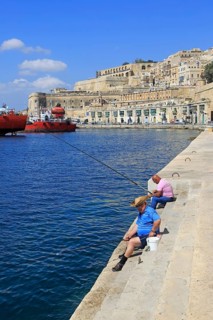 Men fishing historic waterfront buildings on quayside, Valletta, Malta, Europe