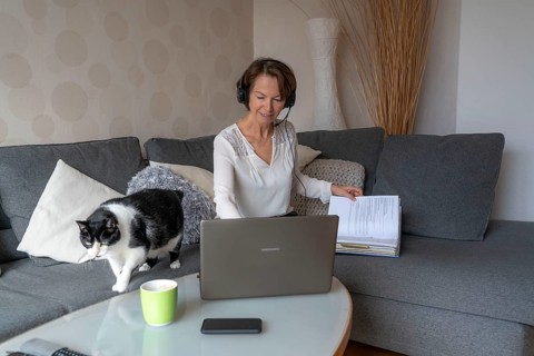 Woman, mid-50s, works from home, with laptop and communicates with colleagues via headset, home