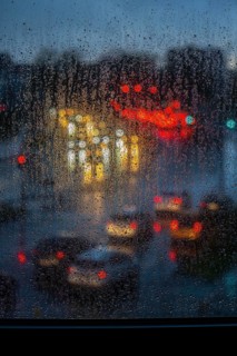 Rainy weather, road traffic, raindrops on a window pane, behind, blurred, lights of vehicles on a