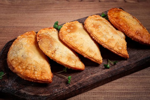 Fried chebureks, deep-fried, mini, on a chopping board, wooden table, close-up, no people