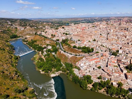 Aerial view of a city with many houses with a river flowing through it, with a bridge and hilly