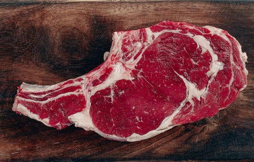 Raw rib eye steak, cowboy steak, wooden chopping board, marble table, top view, no people