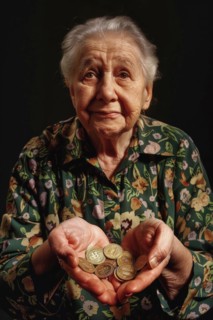 An elderly woman holds coins in both hands and looks sadly into the camera, symbolising poverty in