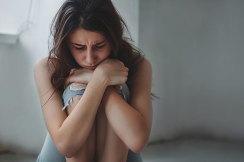 Sad young woman hugging her knees in domestic room. KI generiert, generiert AI generated