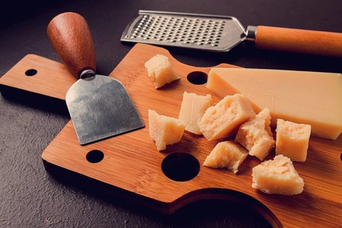 Hard cheese, parmesan, on a cutting board, cheese knife, grater, top view, no people