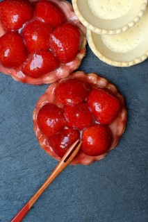 Topped strawberry tartlets with fork and empty tartlet bases