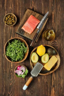 An assortment of fresh ingredients on a wooden surface, including salmon fillet, avocado, lemon,