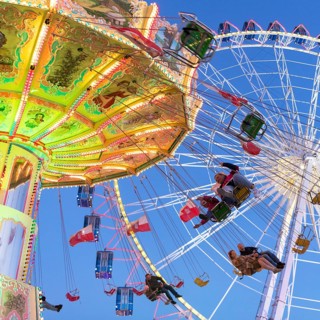 Illuminated chain carousel and Ferris wheel at night with cheerful people, funfair, wave flight,