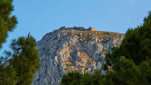 An ancient castle crowning a majestic hilltop, framed by fir trees, Archaic Castle, Akrokorinthos,