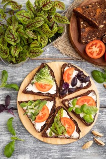 Grain rye bread sandwiches with cream cheese, tomatoes and sorrel microgreen on gray wooden