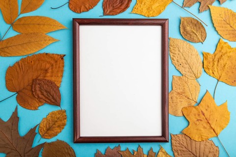 Composition with yellow and brown autumn leaves and wooden frame mockup on blue pastel background.