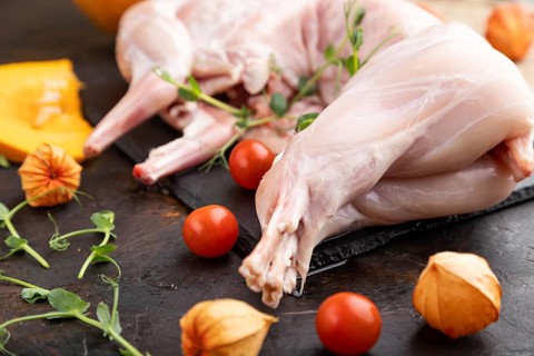 Whole raw rabbit with pumpkin, tomatoes, pea sprouts on a black concrete background and linen