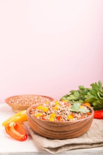 Buckwheat porridge with vegetables in wooden bowl on a pink background and linen textile. Side