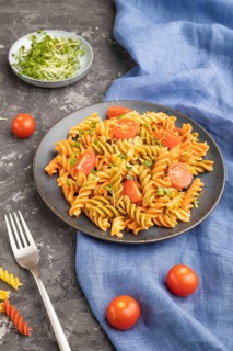 Tortiglioni semolina pasta with tomato and microgreen sprouts on a black concrete background and