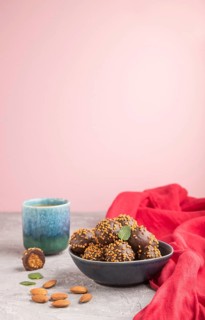 Chocolate caramel ball candies with almonds and a cup of coffee on a gray and pink background and