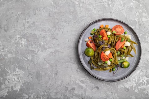 Tagliatelle green spinach pasta with tomato, pea and microgreen sprouts on a gray concrete