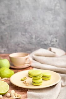 Green macarons or macaroons cakes with cup of coffee on a brown and gray concrete background and