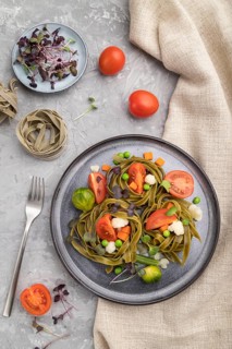 Tagliatelle green spinach pasta with tomato, pea and microgreen sprouts on a gray concrete