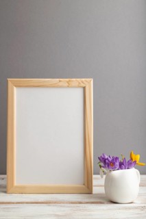Beige wooden frame mockup with snowdrop crocus flowers on gray paper background. Blank, vertical