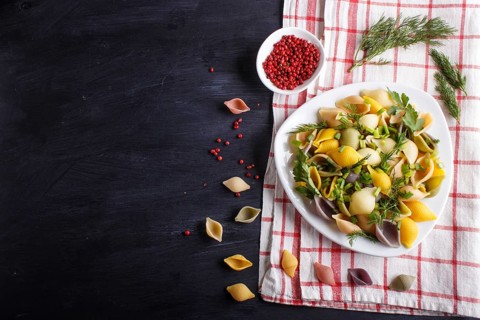 Conchiglie colored pasta with fresh greengrocery on a linen tablecloth on black wooden background.
